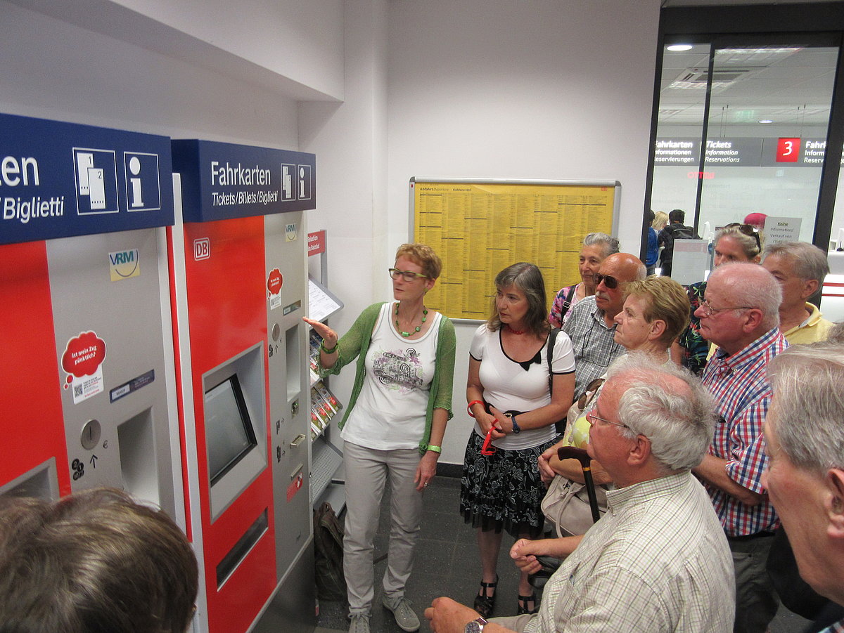Personengruppe steht vor Fahrkartenautomat in einem Bahnhof
